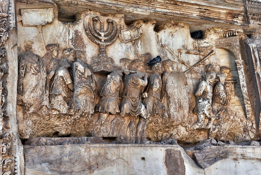 上图：罗马提多凯旋门的浮雕，描绘罗马士兵扛着从耶路撒冷圣殿掳来的金灯台、长号和陈设饼桌。多米田皇帝在他哥哥提多皇帝去世后不久，建了一座大理石单拱凯旋门，以纪念提多率军于主70年摧毁耶路撒冷和第二圣殿，平息了主后66年开始的犹太人起义。直到今天，许多犹太人拒绝从拱门下经过。1948年以色列复国时，大批人群从罗马犹太社区沿着与古罗马凯旋式相反的方向通过提多凯旋门。