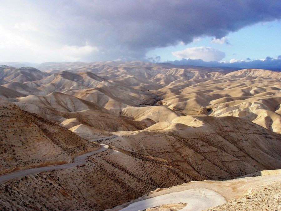上图：犹大旷野位于犹大山地和约旦河谷之间。从橄榄山东面不远处开始就是绵延的山坡，草木稀疏，人迹罕至，从海拔900多米的犹大山地向东一直下降到海平面以下400多米的死海，南北约长100公里，东西宽约20-25公里。犹大旷野的地势由西至东下降约1300米，开始是许多平滑光秃的白垩山头连绵起伏，溪谷与沟壑纵横交错，靠近死海时逐渐变成陡峭的峡谷，到死海边成为嶙峋的悬崖。犹大旷野位于中央山地分水岭以东，地中海的雨云由西吹来，大部份雨水落在分水岭西面，分水岭东面的犹大旷野非常干旱，又有干燥的东风吹刮，雨季才偶尔有阵雨。在雨季的几个星期，干涸的旱溪（Wadi）中会激流奔涌，旷野中会长出少许植物。 大卫曾在犹大旷野躲避扫罗和押沙龙的追杀（撒上二十三14,24；二十四1；撒下十五23），他将犹大旷野描述为「干旱疲乏无水之地」（诗六十三1）。每年赎罪日，「归于阿撒泻勒的山羊」从圣殿被放到犹大旷野（利十六10）。以西结在异象中看见一条溪流从圣殿流出，经过这片旷野，灌溉两岸繁茂的树木（结四十七1-10）。施洗约翰在死海北面的那片犹大旷野开始传道（太三1-6），主耶稣很可能也在犹大旷野受魔鬼引诱（太四1）。